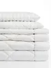 A stack of white bedding items, including pillows and duvets, is neatly arranged against a white background. Produktbild-Vorschau