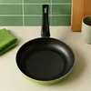 A green frying pan with a black handle is placed on a countertop with green tiles in the background. Produktbild-Vorschau