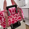 A pink and red leopard print duffel bag is placed on top of a white suitcase, with the suitcase handle protruding through a pocket in the bag. Produktbild-Vorschau