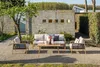 An outdoor lounge set with a sofa and two armchairs is arranged on a gravel patio in front of a textured concrete wall. Produktbild-Vorschau