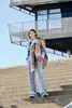 A woman stands on concrete steps in front of a modern building, wearing a colorful scarf. Produktbild-Vorschau