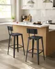 Two black bar stools are placed in front of a kitchen island with a white countertop. The kitchen has white cabinets and a window with natural light. Produktbild-Vorschau