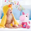 A baby wearing a yellow duck towel is playing with a pink unicorn toy, with musical notes depicted in the air. Anteprima dell’immagine prodotto