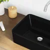 A close-up view of a black ceramic sink on a wooden countertop, with a faucet and a small container of toiletries. Podgląd zdjęcia produktu