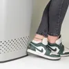 A person's legs and feet wearing sneakers and an anklet are shown next to a light gray laundry basket. Produktbild-Vorschau