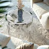 A mirrored round coffee table with a vase of flowers on it, placed on a textured rug in a living room setting with sofas. Anteprima dell’immagine prodotto