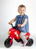 A young child is sitting on a red toy motorcycle. Anteprima dell’immagine prodotto