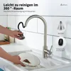 A hand is shown cleaning a dirty plate under a kitchen faucet with a pull-down sprayer. The faucet is made of brushed stainless steel and has a modern design. There are inset images showing features of the faucet. Produktbild-Vorschau