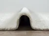 A close-up view of a cream-colored shaggy rug, folded to reveal its texture and underside. Produktbild-Vorschau