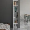 A tall, narrow white bookshelf filled with books and decorative items, placed next to a dark gray wall and a bed. In the background, a dining table with chairs is visible. Produktbild-Vorschau