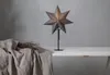 A star-shaped lamp sits on a table next to a bundle of dried branches and draped fabric. Podgląd zdjęcia produktu