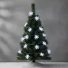A small artificial Christmas tree decorated with snowflake-shaped LED lights, placed on a surface covered in artificial snow. Náhled obrázku produktu