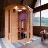 An infrared sauna is set up in a rustic attic room with large windows overlooking a misty landscape. A small wooden stool with a candle and stones sits nearby. Produktbild-Vorschau