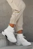 A person wearing white high-top sneakers and beige cargo pants is standing on concrete steps. Produktbild-Vorschau
