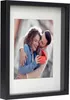 A framed photo of a couple, with the man kissing the woman's cheek as she opens a gift. Produktbild-Vorschau