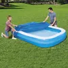 A man and a woman are covering an inflatable pool with a blue tarp in a grassy backyard. Produktbild-Vorschau