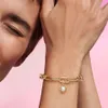 A close-up shot of a person's arm wearing a gold charm bracelet with a pearl sun charm. Produktbild-Vorschau