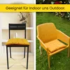 A split image showing two chairs with yellow cushions. One chair is indoors on a wooden floor with shelves in the background, and the other is outdoors on grass with flowers in the background. Produktbild-Vorschau