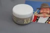 A jar of hair product is placed on a gray surface in front of a photograph of a man with a large beard wearing a hat and traditional clothing. Produktbild-Vorschau