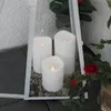 Three white LED candles are placed inside a white lantern on a bed of small gray stones. Red roses and green leaves are visible to the right of the lantern. Produktbild-Vorschau