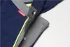 A close-up view of a navy blue work garment with gray and yellow accents, showing a snap closure and a brand tag. Produktbild-Vorschau