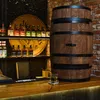 A wooden barrel-shaped cabinet is displayed on a wooden bar counter, with shelves of liquor bottles in the background. Náhled obrázku produktu