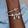 A close-up shot of a person's arm wearing two silver Pandora charm bracelets. Podgląd zdjęcia produktu