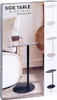 The image shows the packaging of a side table, with a lifestyle shot of the table in use on the front. There are also smaller images of different color options for the table on the right side of the packaging. Voir les images du produit