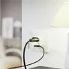 A close-up of a white wall outlet with a black adapter plugged in, and a black cable connected to it. A lamp shade is visible in the upper right corner. Produktbild-Vorschau