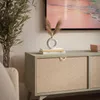 A close-up shot of a TV cabinet with a herringbone pattern on the doors, decorated with a vase and books. Produktbild-Vorschau