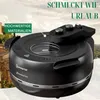 A black pizza oven is shown in front of a background depicting a Tuscan landscape with buildings and a cloudy sky. Produktbild-Vorschau