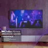 A television screen displaying a concert scene, with text overlays promoting Dolby Atmos immersive sound. Produktbild-Vorschau