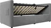The image shows the underside of a grey upholstered bed frame with the mattress support mechanism open, revealing wooden slats and hydraulic lifts. A small grey fabric pocket is visible on the side of the headboard. Anteprima dell’immagine prodotto