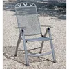 A metal folding chair sits on a gravel surface, with shadows cast by trees overhead. Produktbild-Vorschau