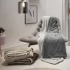 A cozy living room scene with blankets draped over a chair and stacked on the floor. Produktbild-Vorschau