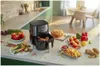 A kitchen counter displaying various foods and a black air fryer. Produktbild-Vorschau