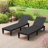 Two black plastic sun loungers are placed on a wooden deck in a garden setting, with lush green foliage and flowering plants in the background. Produktbild-Vorschau