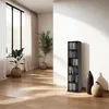 A tall, narrow black CD/DVD shelf unit filled with media is placed against a white wall in a room with wooden floors and large windows with white curtains. Two decorative vases and a potted plant are also visible. Produktbild-Vorschau
