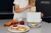 A person is putting bread into a white toaster, with fruit and toast with toppings on the counter. Anteprima dell’immagine prodotto