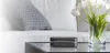 A modern living room setting with a couch, a coffee table, and a vase of flowers. Produktbild-Vorschau