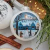 A close-up of a Christmas ornament depicting a winter village scene with people building a snowman. Náhľad obrázku produktu
