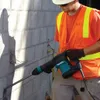 A construction worker wearing a safety vest and hard hat is using a demolition hammer on a concrete block wall. Anteprima dell’immagine prodotto