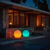 Two illuminated spheres, one orange and one cyan, sit on the ground in front of a modern house at dusk. Produktbild-Vorschau