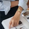 A person's arm wearing a gold watch is resting on an open book. Produktbild-Vorschau