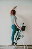 A woman is painting a wall while standing on a stepladder. Voir les images du produit