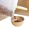 Cereal being poured from a clear plastic container into a tan bowl. Produktbild-Vorschau