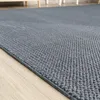 A close-up view of a textured gray rug on a light wooden floor. Produktbild-Vorschau