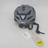 A gray Uvex bicycle helmet with yellow accents and straps is shown on a white and light gray background. Several tags are attached to the helmet. Produktbild-Vorschau