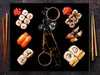 A collection of sushi dishes arranged around an anime character illustration on a black surface, with chopsticks on the sides. Produktbild-Vorschau
