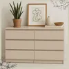 A beige dresser with six drawers is shown in a room setting, with decorative items on top. Produktbild-Vorschau